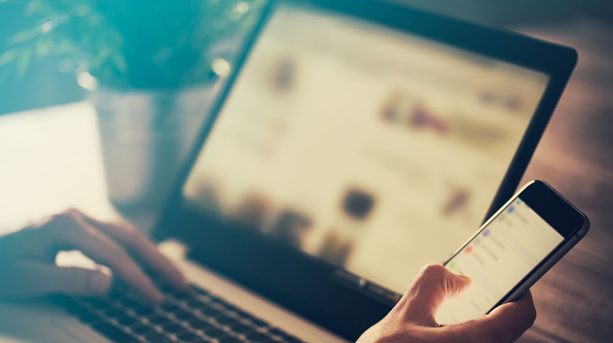 A person looking at their phone and using a laptop