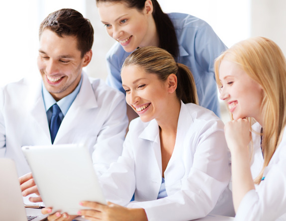 Four aesthetic professionals looking at medical spa software on a tablet and computer.