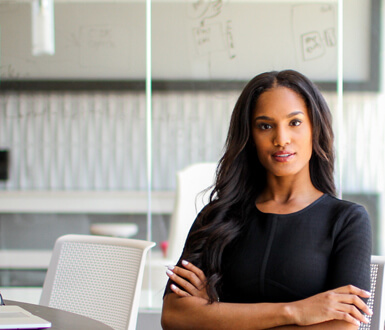 Businesswoman sitting at a desk, engaging directly with the viewer, with an open laptop on the desk in front of her, representing the professionalism and reliability of the best medical spa software of 2024