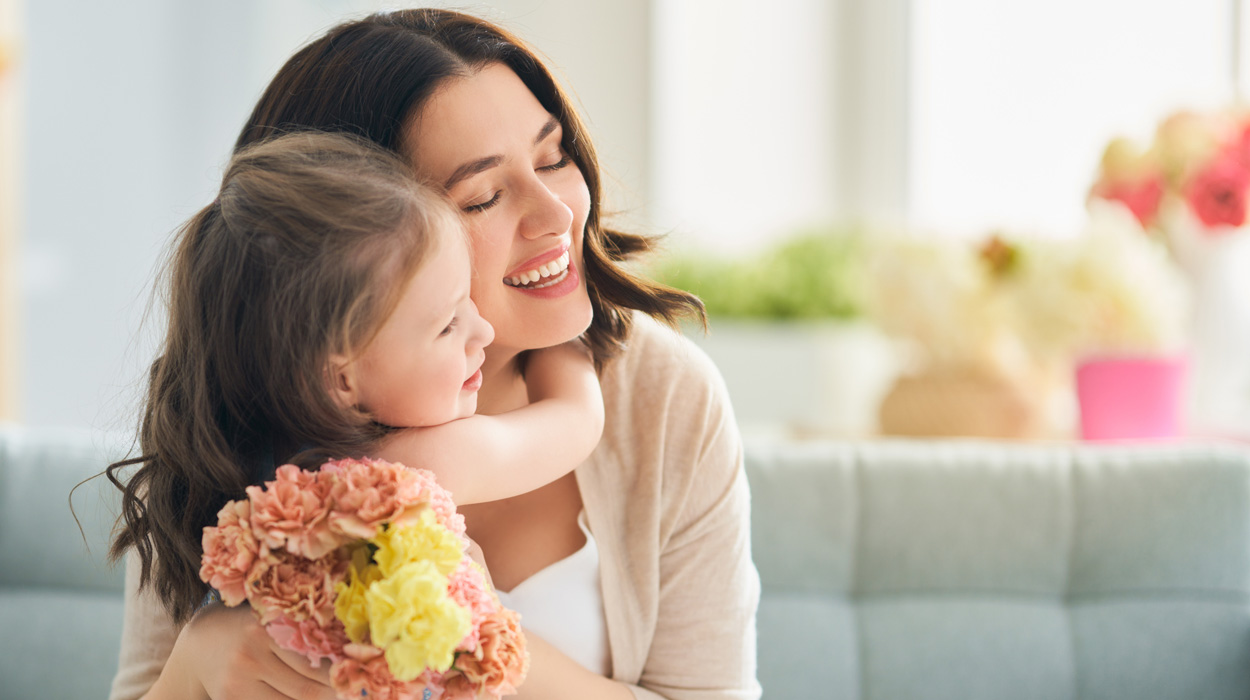 Little girl gifting her mother flowers while hugging her.