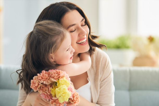 Little girl gifting her mother flowers while hugging her.