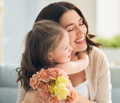 Little girl gifting her mother flowers while hugging her.