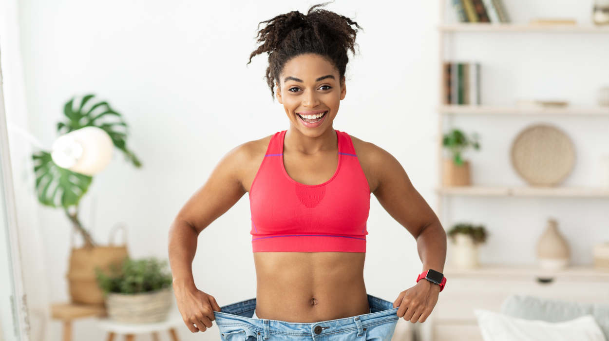 Happy woman celebrating weight loss success holding oversized jeans showing post-bariatric surgery transformation results