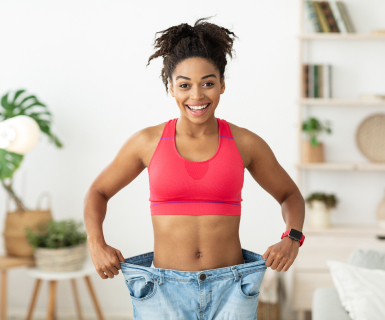 Happy woman celebrating weight loss success holding oversized jeans showing post-bariatric surgery transformation results