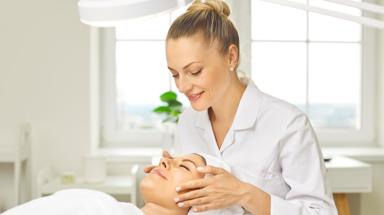 Medspa aesthetician using medi spa management software while performing a facial treatment on a happy client.