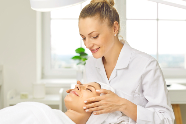 Medspa aesthetician using medi spa management software while performing a facial treatment on a happy client.