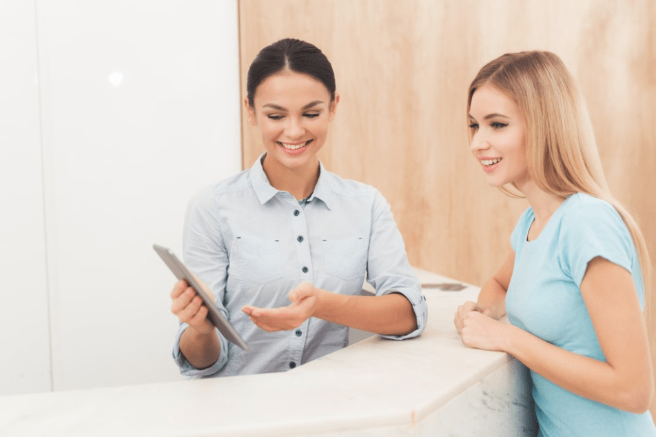 Text: Medspa front office team member showing services menu to client on a tablet.