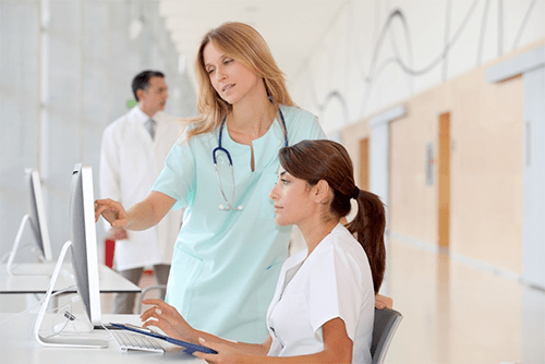 Nurse working with employee in front of computer