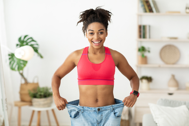 Happy woman celebrating weight loss success holding oversized jeans showing post-bariatric surgery transformation results